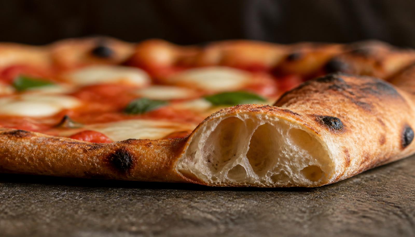 Cornicione dorato e alveolato di una pizza margherita fotografato dal basso